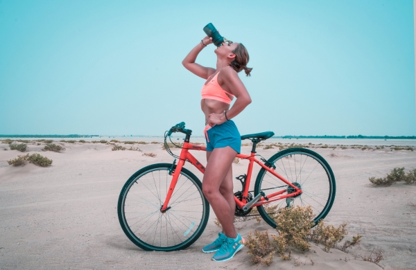 Woman with her bike on the beach and drinking water